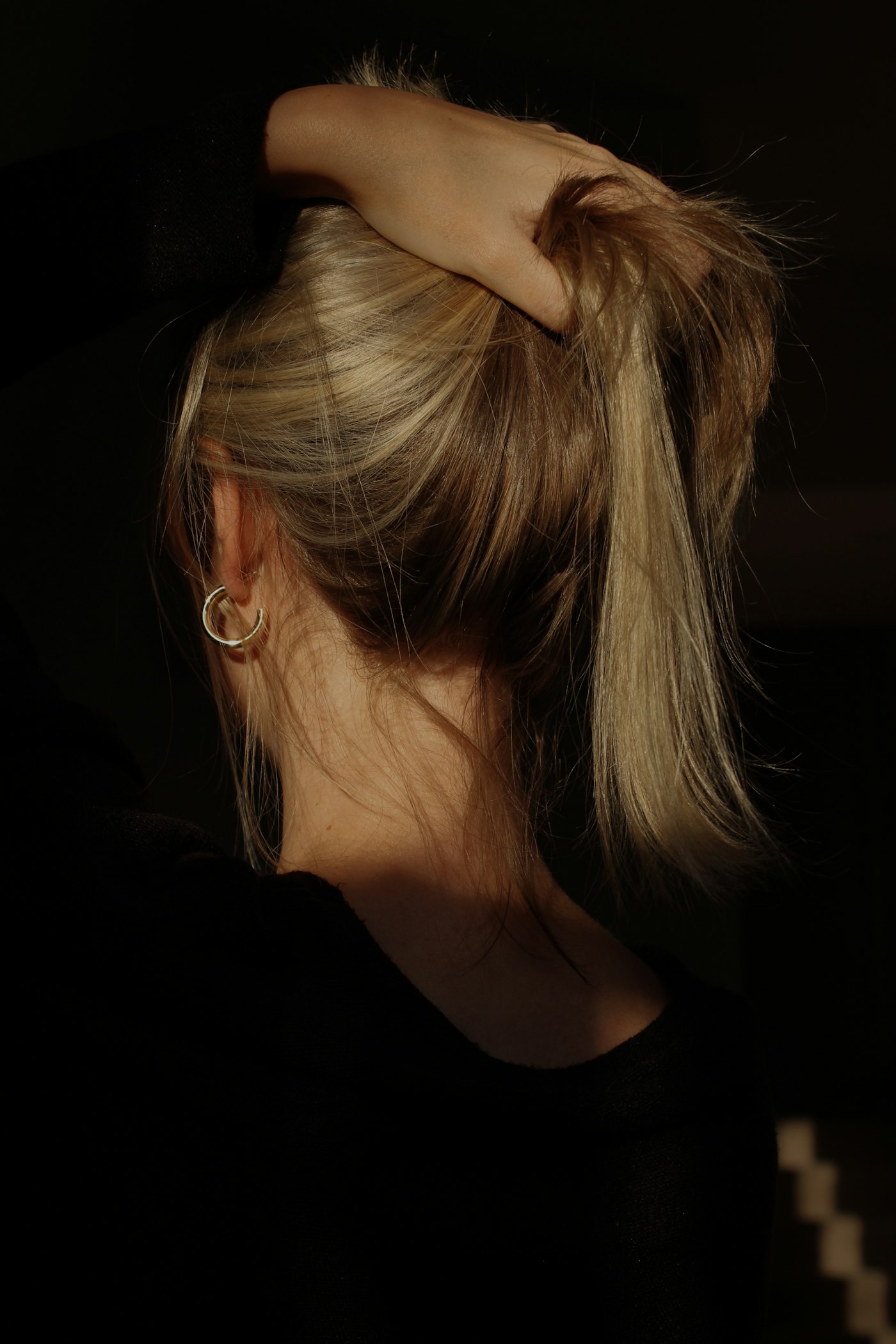 Cheveux blonds relevés en queue de cheval, vus de dos, lumière sombre