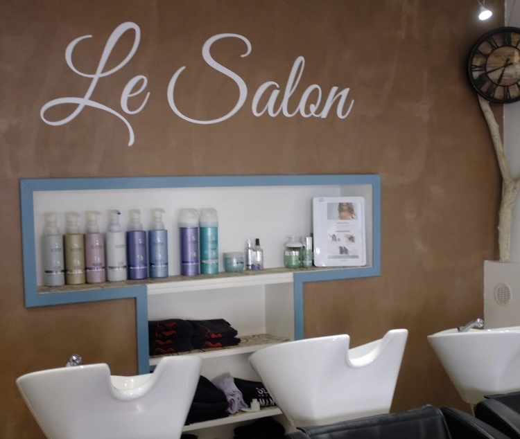 L’intérieur du salon : mur cuivré, étagère de produits, bacs de lavage blancs et lettrage « Le Salon »